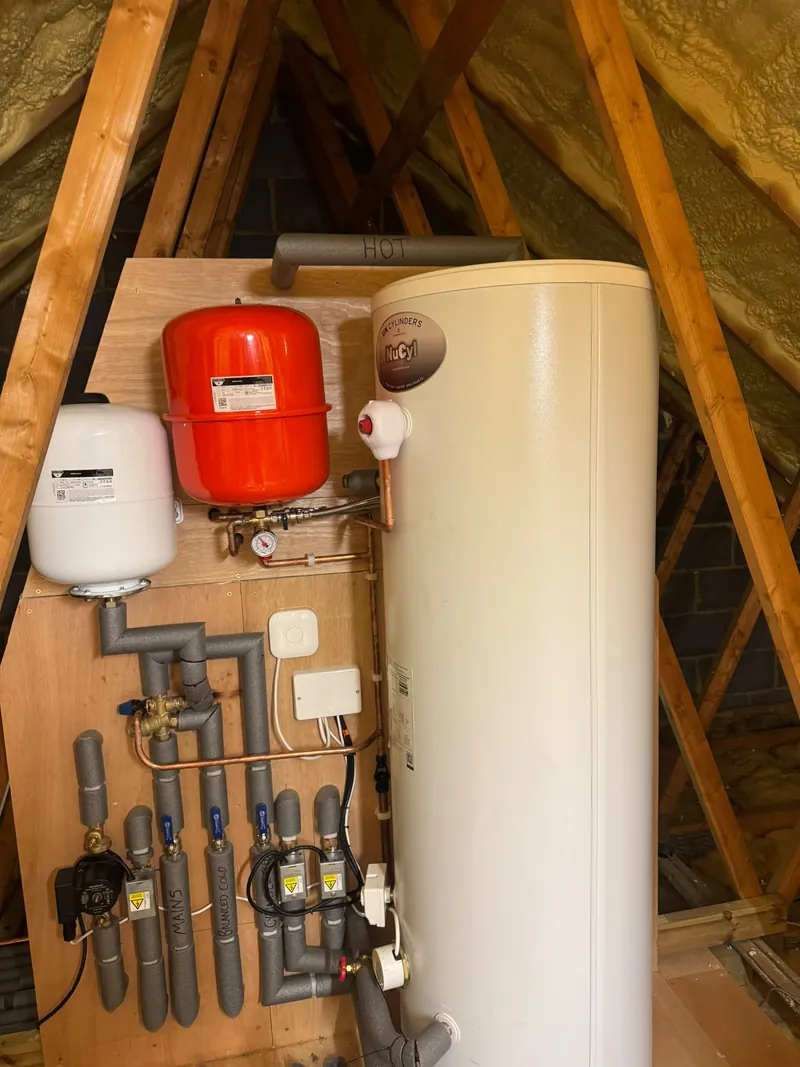 A hot water cylinder, expansion vessels and insulated pipework in a loft