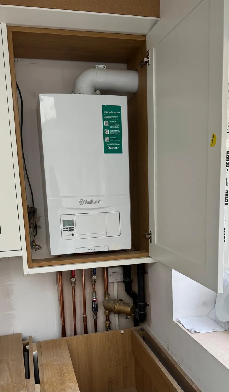A white boiler in an open cabinet with a flue and copper pipework