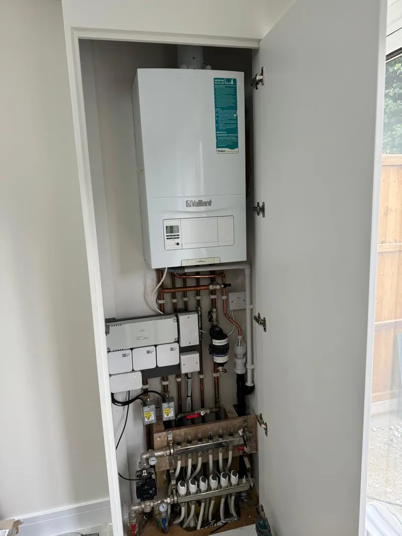 A boiler, heating controls and pipework inside an open cupboard