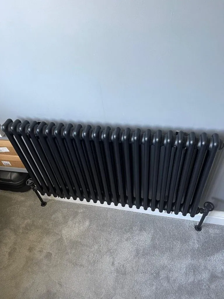 Black column radiator fitted against a light-coloured wall